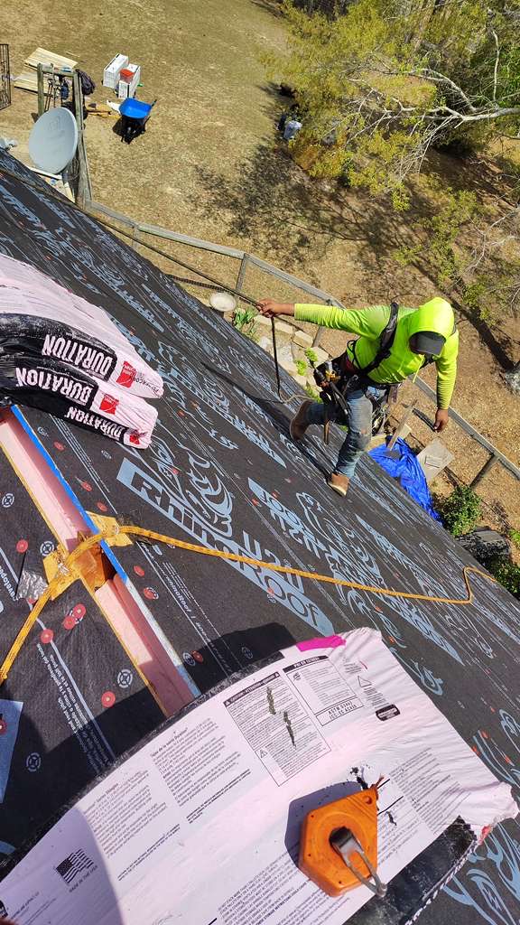 Exterior Genie roofer installing synthetic underlayment with safety harness on a Lexington SC home